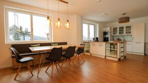 A modern kitchen with wooden flooring, a dining area with a wooden table and chairs, and a view of the outdoors through large windows. - Ferienwohnung mit Terrasse (Neuhaus an der Triestin)