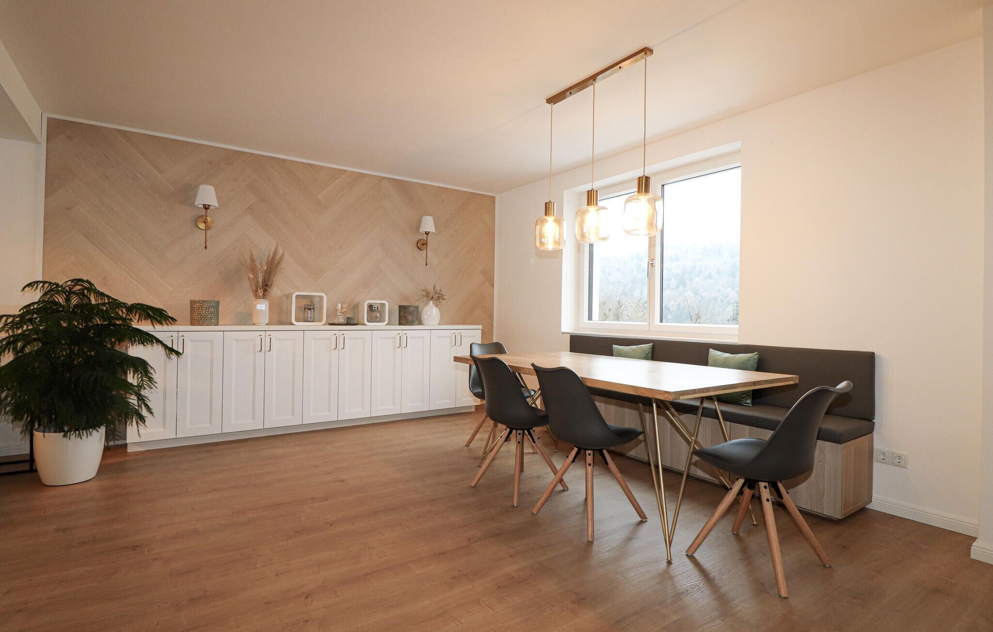 Een moderne keuken met witte kastjes, een houten visgraatvloer en hanglampen.