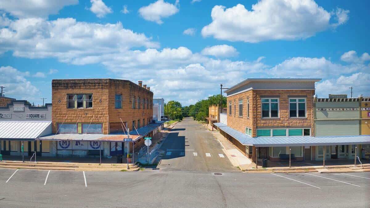 A street view with a row of buildings, including a bank and a store with a blue awning.