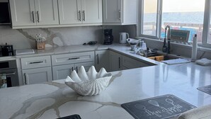 A modern kitchen with white cabinets, a marble countertop, and a view of the ocean. - Stunning Ocean Views! 2-bedroom house, private beach in Melbourne Beach, FL (Melbourne Beach)