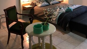 Un dormitorio con cama, una silla, una mesa con cestas verdes y un candelabro.