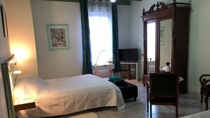 Un dormitorio con cama, mesita de noche, silla, televisor, armario y un pequeño escritorio con silla.