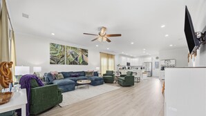 Ein modernes Wohnzimmer mit einer Eckcouch, einem Couchtisch und einem Essbereich mit Stühlen, im Hintergrund eine Küche.