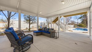 Eine überdachte Terrasse mit Korbmöbeln, einem Pool und einer Treppe zu einer Dachterrasse.