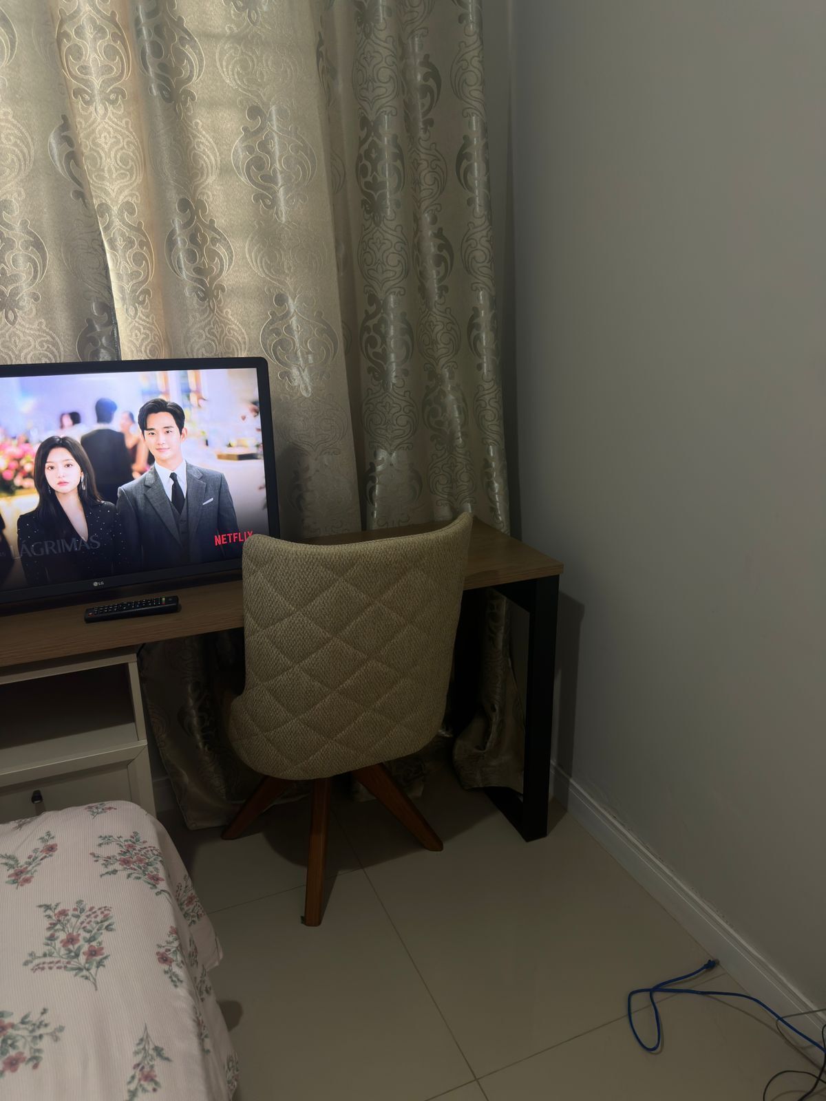 A bedroom with a bed, a TV on a wooden stand, a chair, and a curtain.