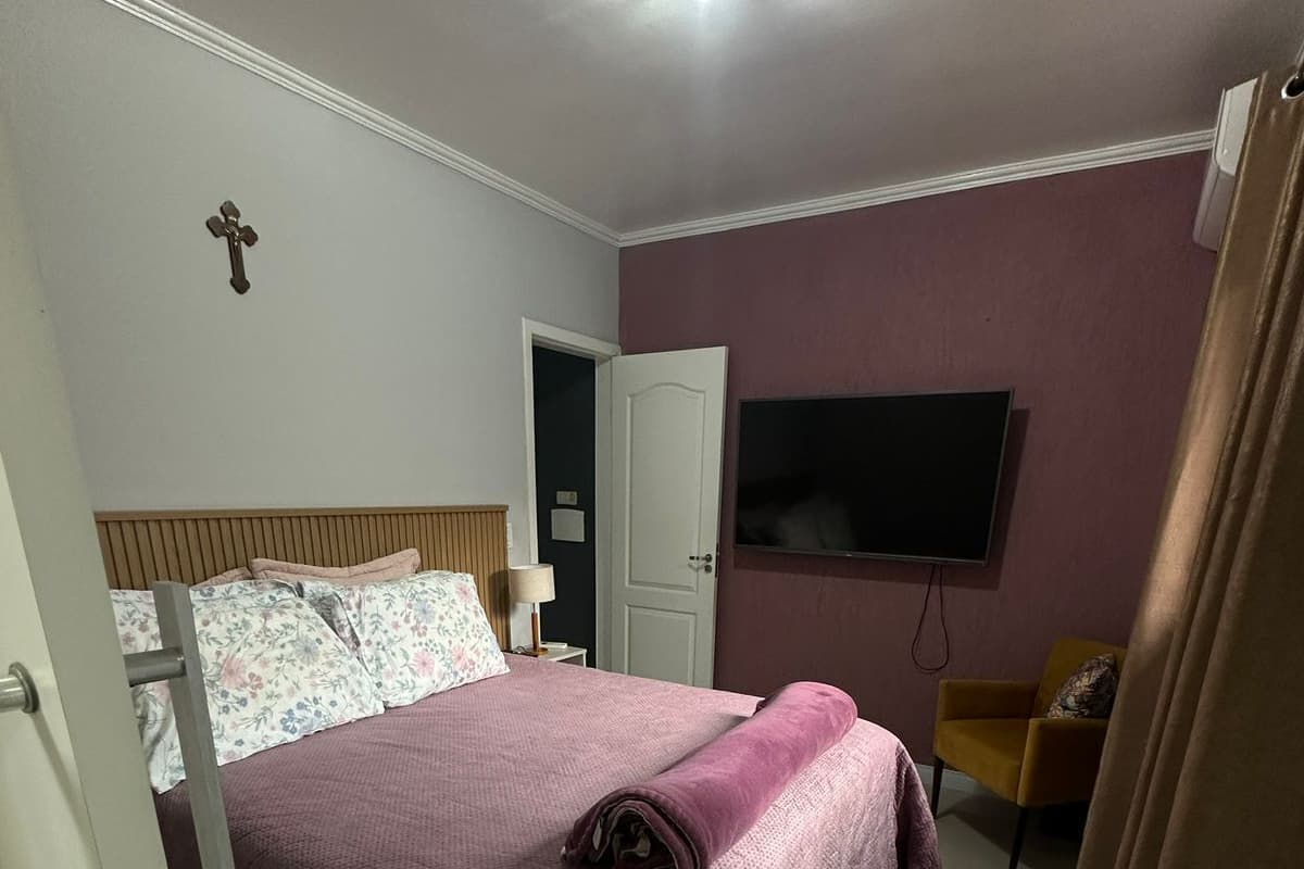 Quarto com uma cama, televisão, porta e uma cadeira.
