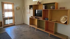 A room with a wooden TV stand, a television, and a door with a glass panel. - La Palomita - Modern Casita in the Heart of Marfa TX (Marfa)