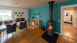 Un salon moderne avec un plancher en bois, un coin repas avec une table et des chaises, un poêle à bois noir, des murs de couleur turquoise et une fenêtre offrant une vue agréable.