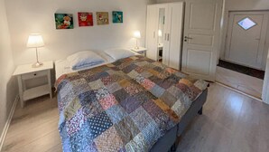 Une chambre à coucher comprenant un lit, deux tables de chevet, une commode, une armoire et une porte avec une petite fenêtre.
