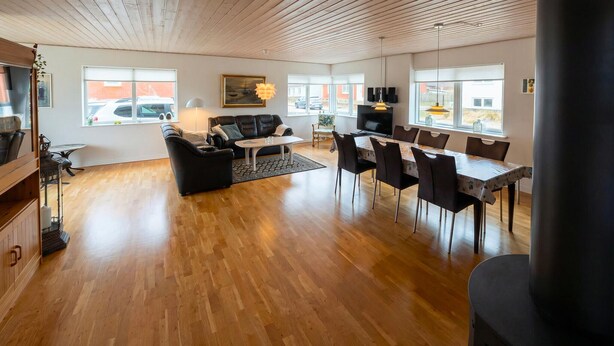 Un vaste espace de vie doté d’un plancher en bois, d’un canapé en cuir noir, d’une table à manger avec des chaises et d’une grande fenêtre offrant une vue sur l’extérieur.