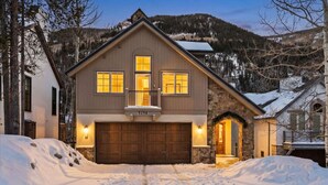 A two-story house with a stone facade, a wooden garage, and a snow-covered driveway. - Spruce Street Chalet | Cozy Mountain Living (Vail)