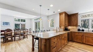 A spacious kitchen with wooden cabinets, a large island, and a dining area with chairs. - Spruce Street Chalet | Cozy Mountain Living (Vail)