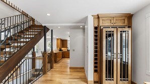 A spacious hallway with a wooden staircase and a large wooden cabinet with glass doors. - Spruce Street Chalet | Cozy Mountain Living (Vail)
