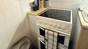 A compact kitchen with a white stove, a small trash bin, and a countertop with kitchen utensils. - Quiet King’s Cross flat – Steps from the Station (London)