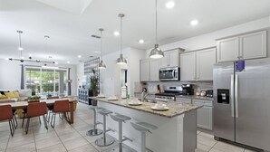 A modern kitchen with stainless steel appliances, a central island with bar stools, and pendant lighting. - Enchanted Palms Villa 7BR w Private Pool (Davenport)