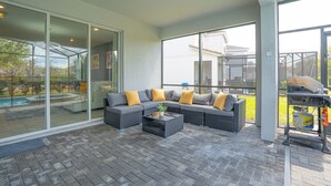 A covered patio with a sectional sofa, a coffee table, and a grill area. - Enchanted Palms Villa 7BR w Private Pool (Davenport)