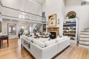 Un vaste salon doté d’un haut plafond, d’une cheminée, d’une grande bibliothèque et d’un escalier menant à l’étage sup érieur.