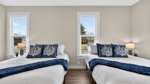 Ein Hotelzimmer mit zwei Betten, jeweils mit weißer Bettwäsche und dunkelblauen Zudecken. Zwei Fenster mit weißen Rahmen und ein Holzboden gehören zur Ausstattung des Raumes.