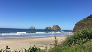 Ein Strand mit drei markanten Felsen in der Ferne, einem sandigen Ufer und einer grasbewachsenen Klippe auf der rechten Seite.