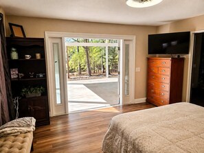 Quarto com cama, cômoda, televisão e porta de vidro deslizante para área externa.