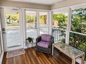 Uma sala de sol com uma cadeira de vime, uma mesa de vidro e vista para o exterior.