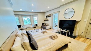 A modern bedroom with a large bed, a flat-screen TV, and a window with a view of trees. - Luxury Waterfront Estate · Sleeps 18 · 45-Min Drive to FIFA World Cup Stadium (East Rutherford)