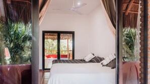 A bedroom with a bed, a ceiling fan, and a view of an outdoor area with plants. - Casa Roja · Whole Home with Pool, Terrace & Palapa · Local Sayulita (Sayulita)