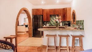A modern kitchen with wooden cabinets, a stainless steel refrigerator, a built-in oven, and a bar area with stools. - Casa Roja · Whole Home with Pool, Terrace & Palapa · Local Sayulita (Sayulita)