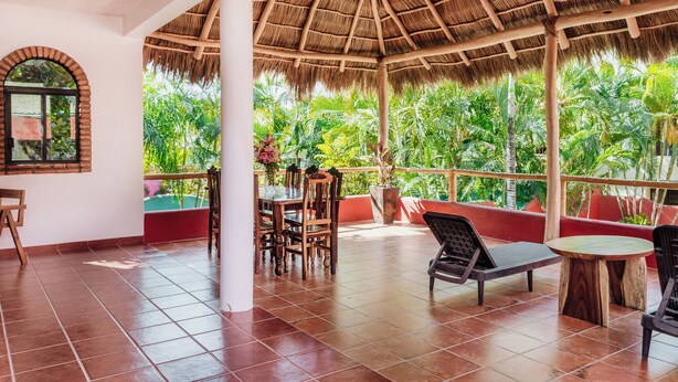 A covered patio with a thatched roof, wooden furniture, and a view of lush greenery. - Casa Roja · Whole Home with Pool, Terrace & Palapa · Local Sayulita (Sayulita)