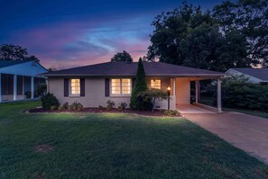 A two-story house with a covered porch, a well-maintained lawn, and a clear sky at dusk.