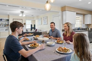 Eine Familie isst an einem Tisch in einer modernen Küche mit weißen Schränken und einem Kronleuchter.