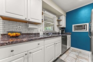 A kitchen with white cabinets, a granite countertop, a microwave, and a blue accent wall. - Soul House • A Music Lover's Retreat • Sleeps 7 (Memphis)