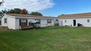 A single-story mobile home with a fenced yard, a bench, and a covered outdoor seating area.