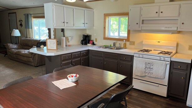 A kitchen with a wooden table, dark cabinets, a white stove, and a window with a view of trees.