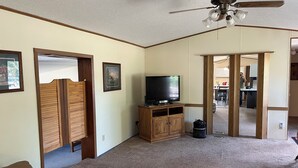 A living room with a ceiling fan, a television on a wooden stand, a brown leather couch, and a carpeted floor.