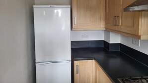 Una cocina con un refrigerador blanco, armarios de madera, una encimera negra y una estufa.