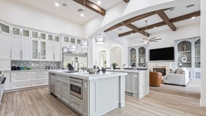 Une cuisine spacieuse avec des meubles blancs, un grand îlot central et un ventilateur de plafond.