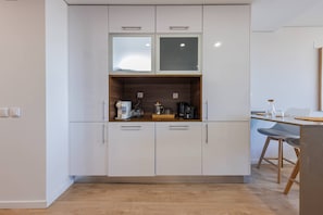 A modern kitchen with white cabinets, a wooden countertop, and a dining area with a chair and table. - 182 Sunset Duplex - by Feeling Inn (Cascais)