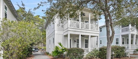 A two-story white building with a balcony, surrounded by trees and a pathway.