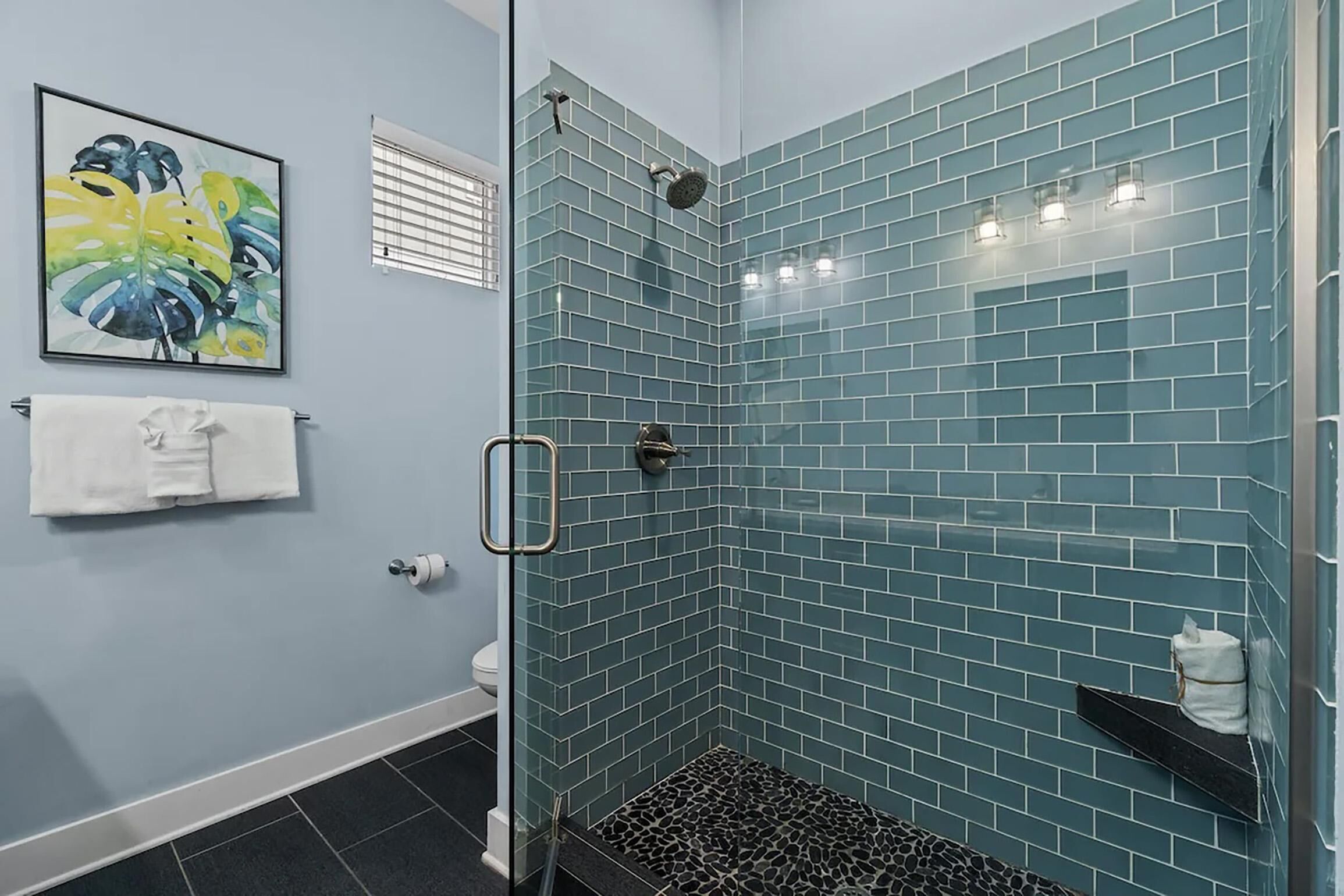 Un baño con ducha de vidrio, paredes con azulejos, inodoro y toallero.