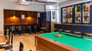 Una mesa de billar con bolas, una mesa de pool y una zona de bar con botellas.