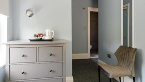 Una habitación con una pared azul claro, un aparador blanco con cajones, una tetera blanca y una silla con respaldo acolchado.