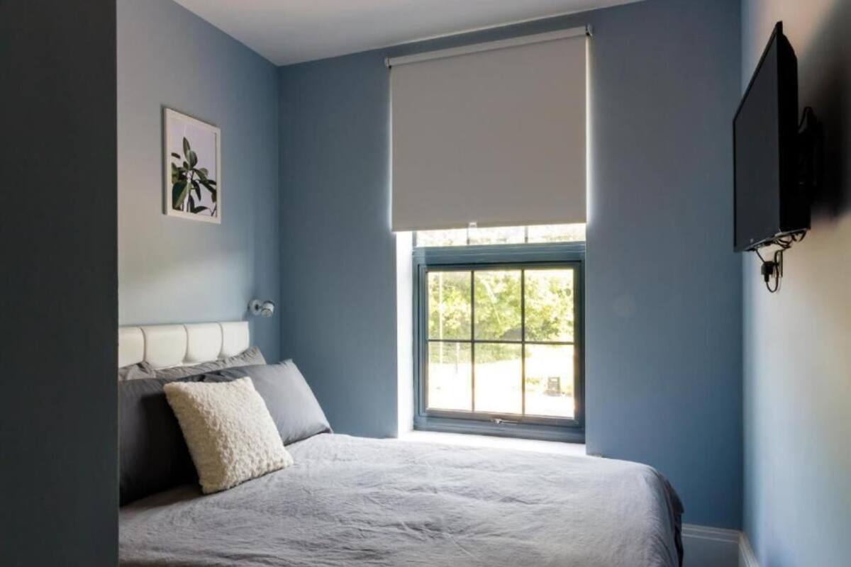 Un dormitorio con una cama, una ventana con cortina, un televisor montado en la pared y un cuadro enmarcado.