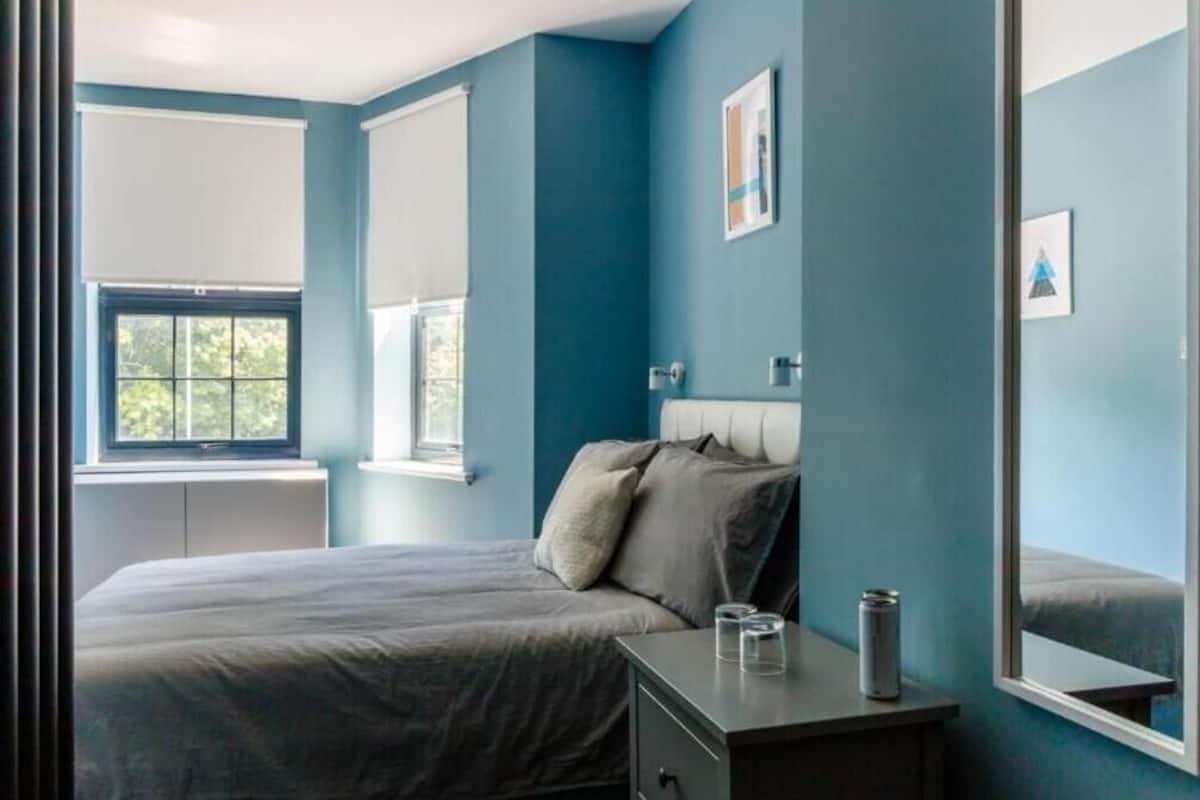 Un dormitorio con cama, mesita de noche y ventana con persianas.