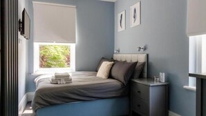 Un dormitorio con cama, mesita de noche y ventana con persianas.