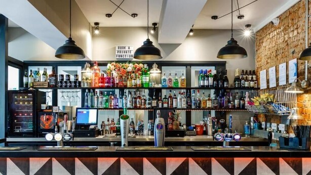 Zona de bar con estantes llenos de botellas de licores, una caja registradora y un cartel que indica reservas para eventos privados.
