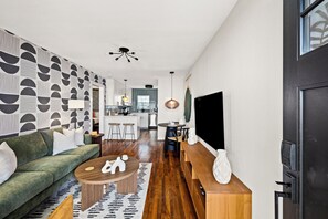 A modern living room with a green sofa, a coffee table, and a patterned wall. - BohoBungalow2- RODEO/Central/MedCenter/DT/GeorgeRBrownConvention/ToyotaCenter (Houston)