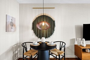 A dining area with a round table, two chairs, a hanging light fixture, and a wall-mounted television. - BohoBungalow2- RODEO/Central/MedCenter/DT/GeorgeRBrownConvention/ToyotaCenter (Houston)