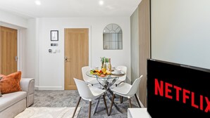 Ett modernt vardagsrum med en matplats, en platt-TV och en väggklocka.