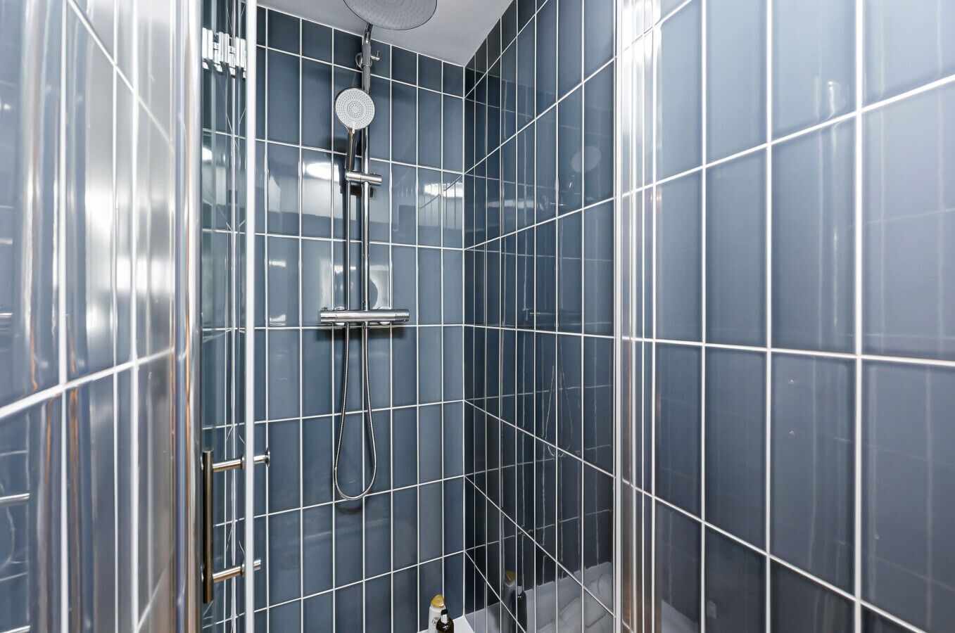 Ein modernes Badezimmer mit blau gefliesten Wänden, einer Duschkabine aus Glas und einem sichtbaren Toilettenpapierhalter.